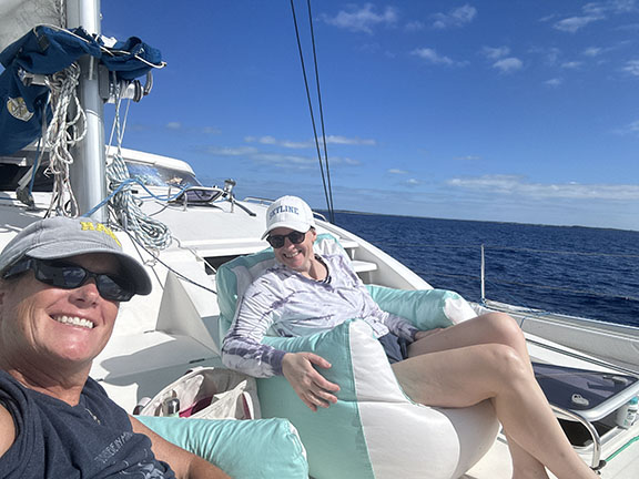 Two guests relaxing comfortably on mint green bean bag chairs on the deck of Bon Bida catamaran, with white sail and rigging visible against blue sky and ocean, perfectly demonstrating the abundant downtime and peaceful relaxation that flows naturally during Breaking Free Sailing charters