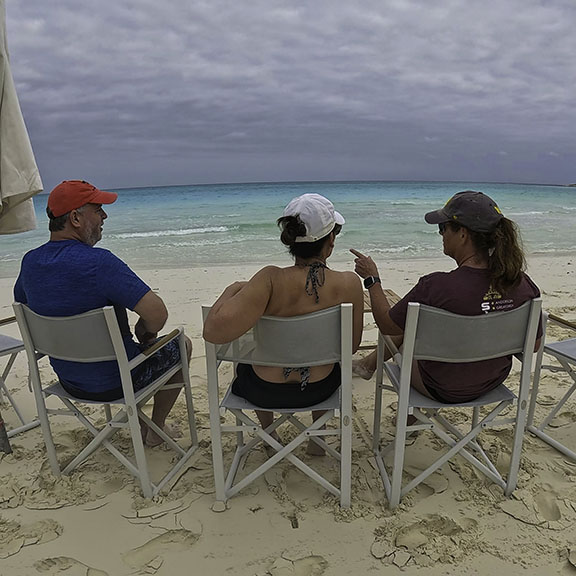 Aerial view of Bon Bida white catamaran anchored in crystal-clear turquoise waters near pristine uninhabited island with white sand beach and lush green vegetation - showcasing the remote destinations accessible on Breaking Free Sailing adventures