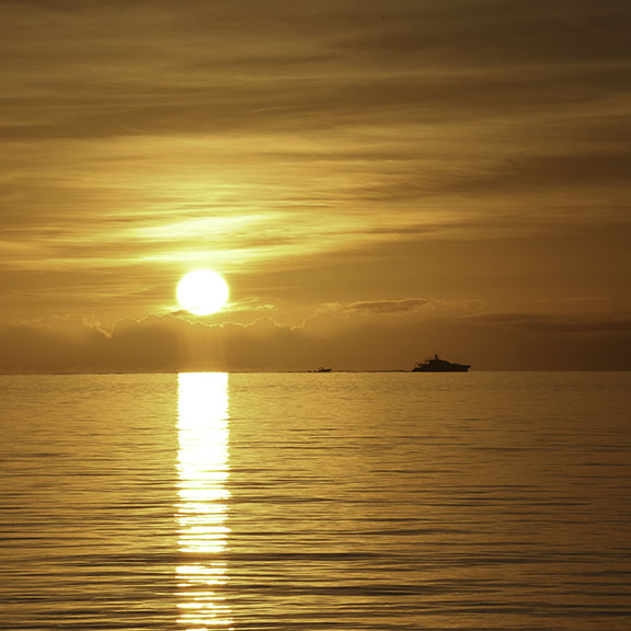 Two guests floating and swimming in incredibly clear shallow turquoise waters with sandy bottom visible beneath them under brilliant blue sky - showcasing the pristine swimming conditions in remote Bahamian locations visited by Breaking Free Sailing