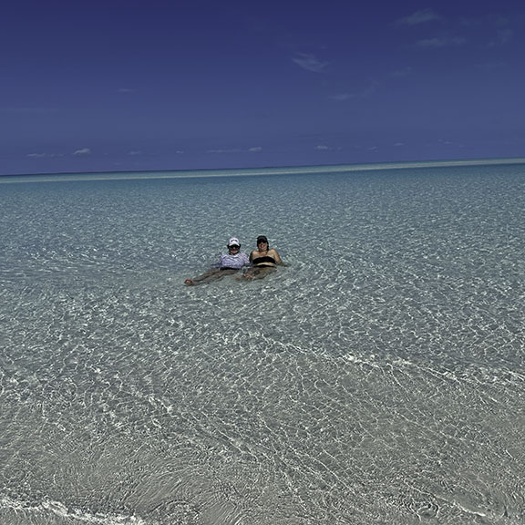 Gray inflatable dinghy with outboard motor floating in crystal-clear turquoise lagoon with guests exploring pristine white sand beach and lush tropical vegetation on remote uninhabited island - showing the exploration opportunities available with Breaking Free Sailing