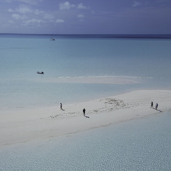 Spectacular golden sunrise over calm ocean waters with bright sun creating golden reflection on water surface and silhouettes of boats in distance under dramatic layered clouds - capturing the breathtaking morning moments on Breaking Free Sailing charters