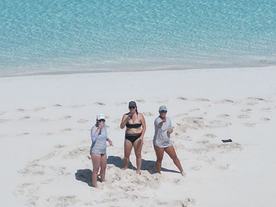 Three guests enjoying pristine white sand beach with crystal clear turquoise waters showing the authentic beach experience of Bahamas sailing